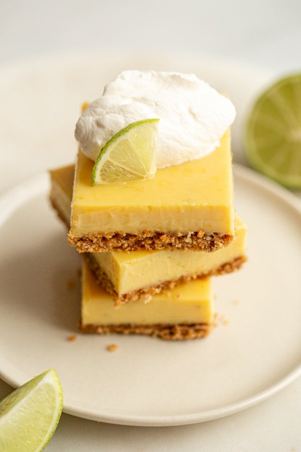 key lime pie bars stacked with fresh whipped cream and a lime