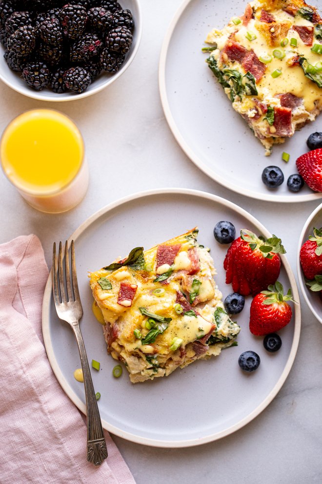 eggs Benedict casserole on a blue plate with fruit and a glass of orange juice