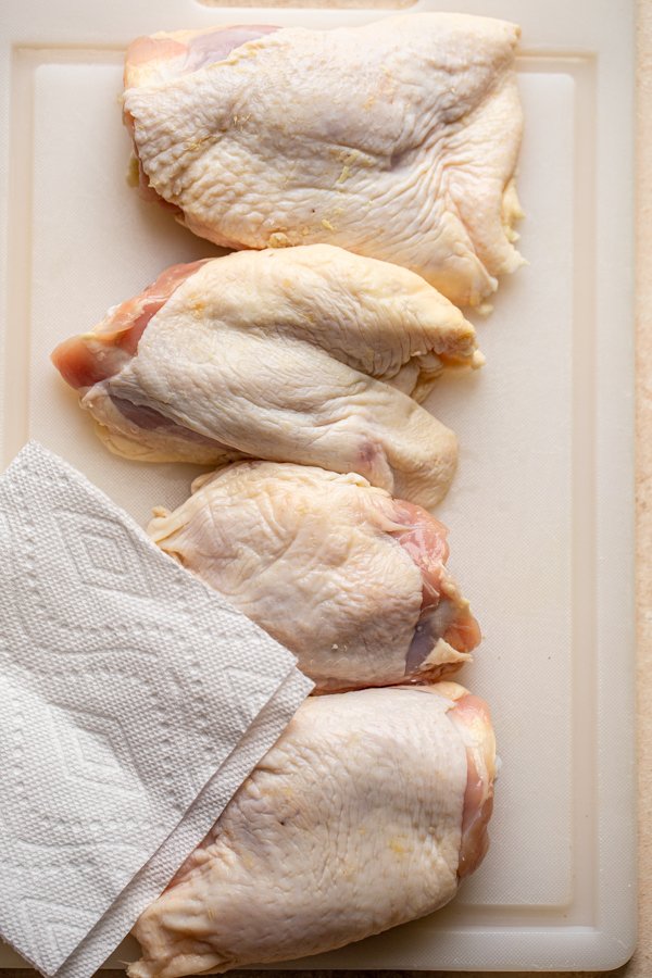 chicken thighs being patted dry on a cutting board