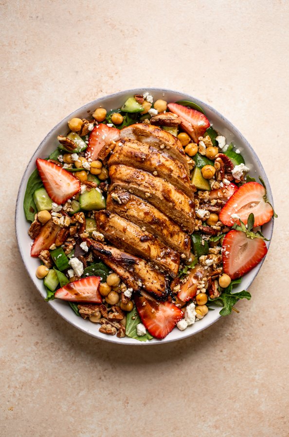 grilled chicken and strawberry salad in a bowl with a fork and a pink napkin