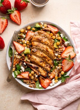 grilled chicken and strawberry salad in a bowl with a fork and a pink napkin