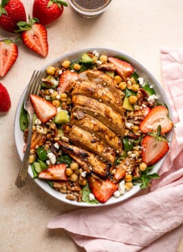 grilled chicken and strawberry salad in a bowl with a fork and a pink napkin