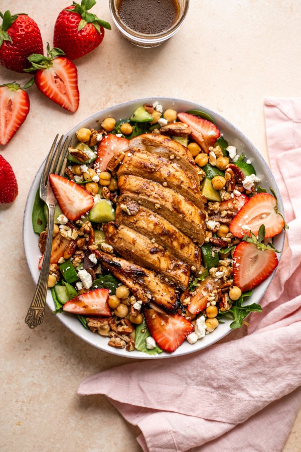 grilled chicken and strawberry salad in a bowl with a fork and a pink napkin