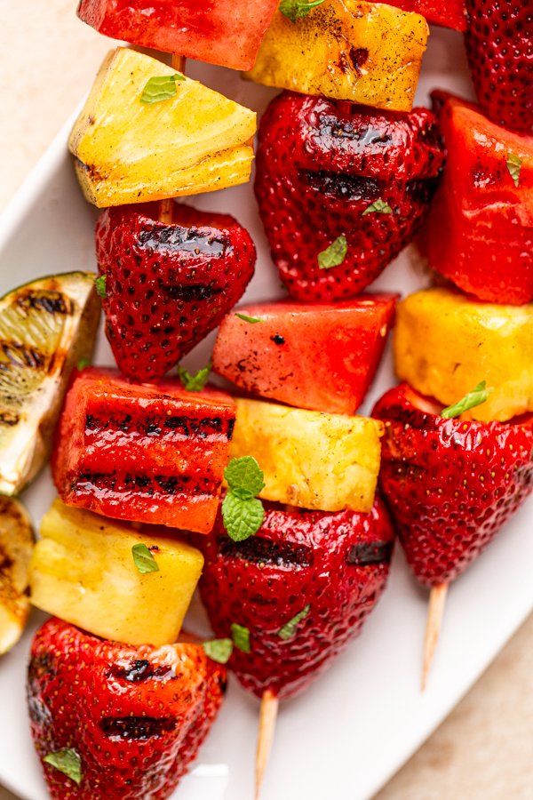 grilled fruit kabobs on a white plate with charred lime