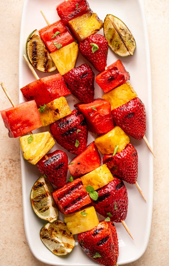 grilled fruit kabobs on a white plate with charred lime