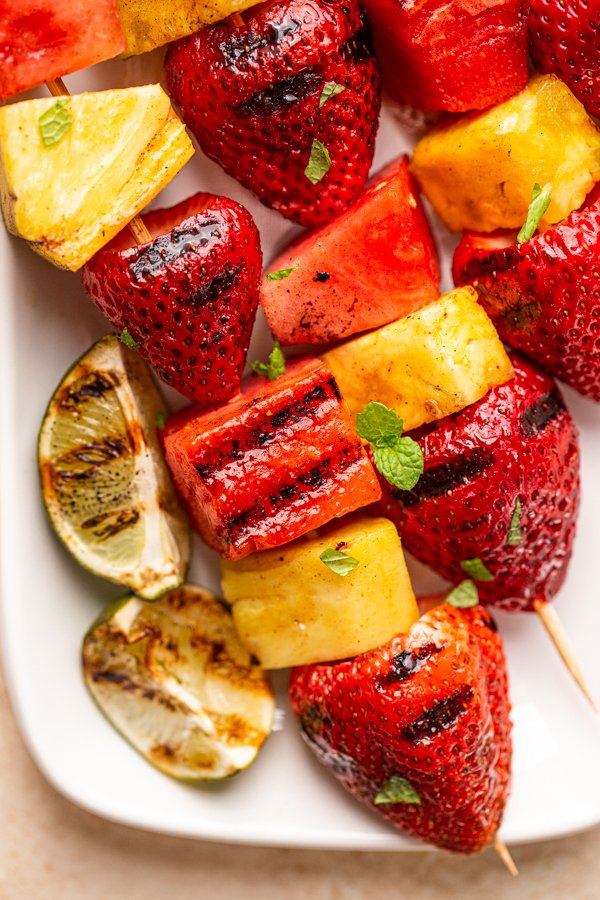 grilled fruit kabobs on a white plate with charred lime