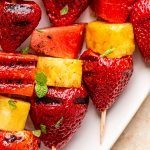 grilled fruit kabobs on a white plate with charred lime