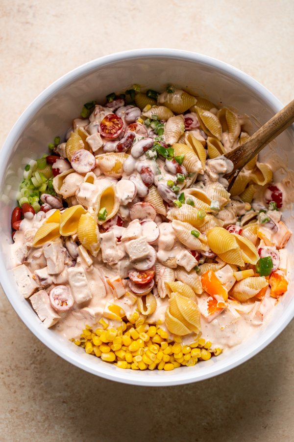 mixing up pasta salad in a big white bowl