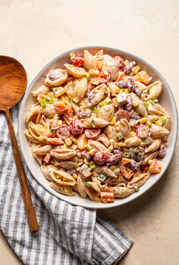 southwest pasta salad in a white bowl with a wood spoon on a cream counter