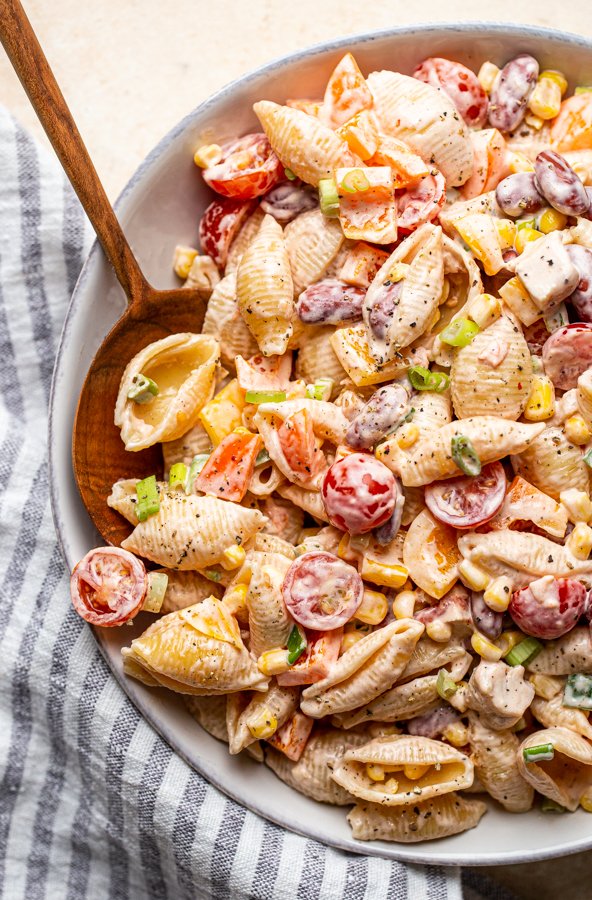 southwest pasta salad in a white bowl with a wood spoon on a cream counter