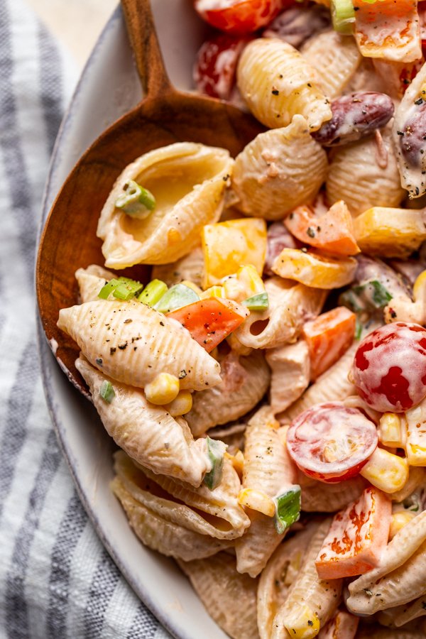 a scoop of southwest pasta salad in a white bowl with a wood spoon on a cream counter