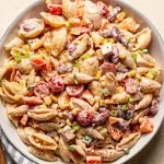 southwest pasta salad in a white bowl with a wood spoon on a cream counter