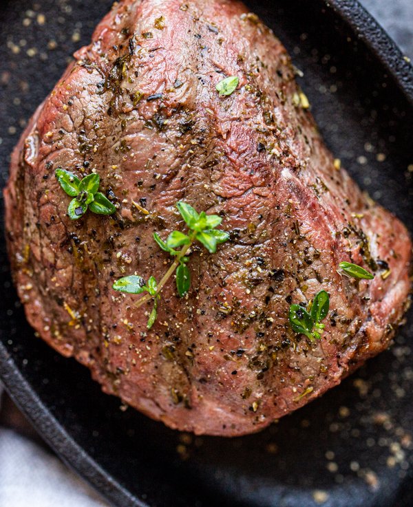 venison steak on a black plate with thyme leaves