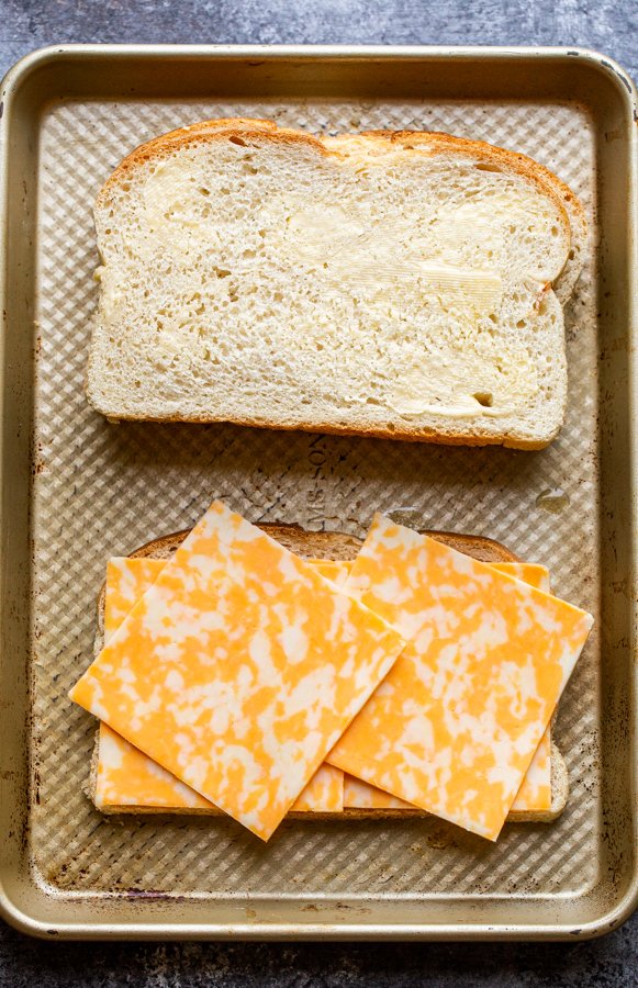 buttered bread and cheese slices on a baking sheet