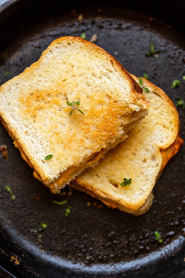 grilled cheese on a black skillet with thyme leaves