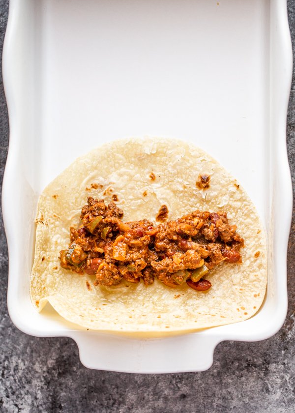 enchilada filling laid in a tortilla in a baking dish