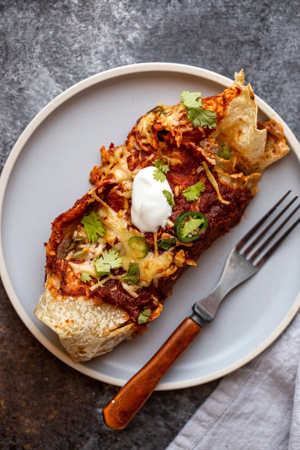 venison enchiladas on a blue plate with a fork and sour cream