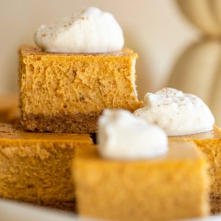 pumpkin cheesecake bars on a platter with whipped cream