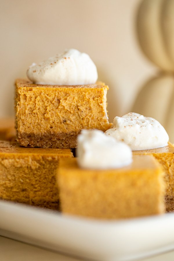 pumpkin cheesecake bars on a platter with whipped cream