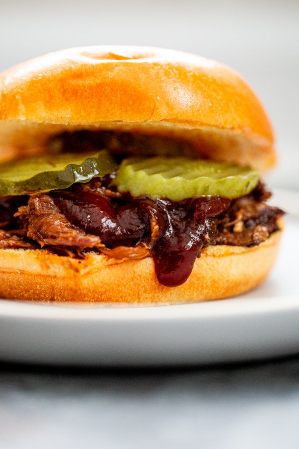 BBQ Venison Sandwich with pickles and sauce on a light blue plate.