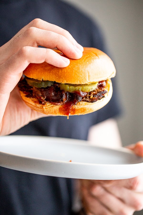 BBQ Venison Sandwich being picked up off of a plate to eat.