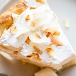 a slice of coconut cream pie on a beige counter with toasted coconut