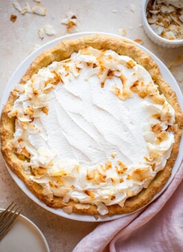 coconut cream pie on a beige counter with toasted coconut and a pink napkin