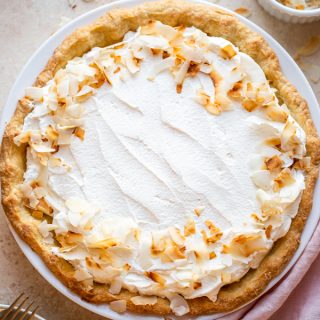 coconut cream pie on a beige counter with toasted coconut and a pink napkin