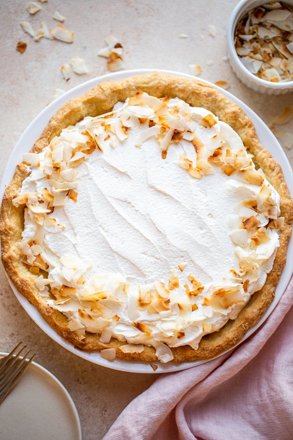 coconut cream pie on a beige counter with toasted coconut and a pink napkin