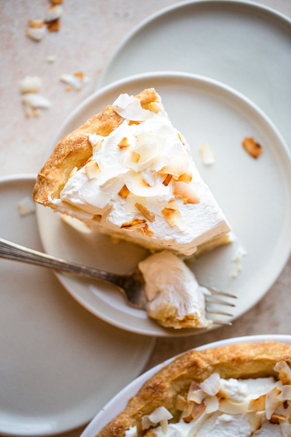 a slice of coconut cream pie on a beige counter with toasted coconut