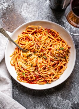 marinara sauce over pasta in a white bowl with wine and a napkin