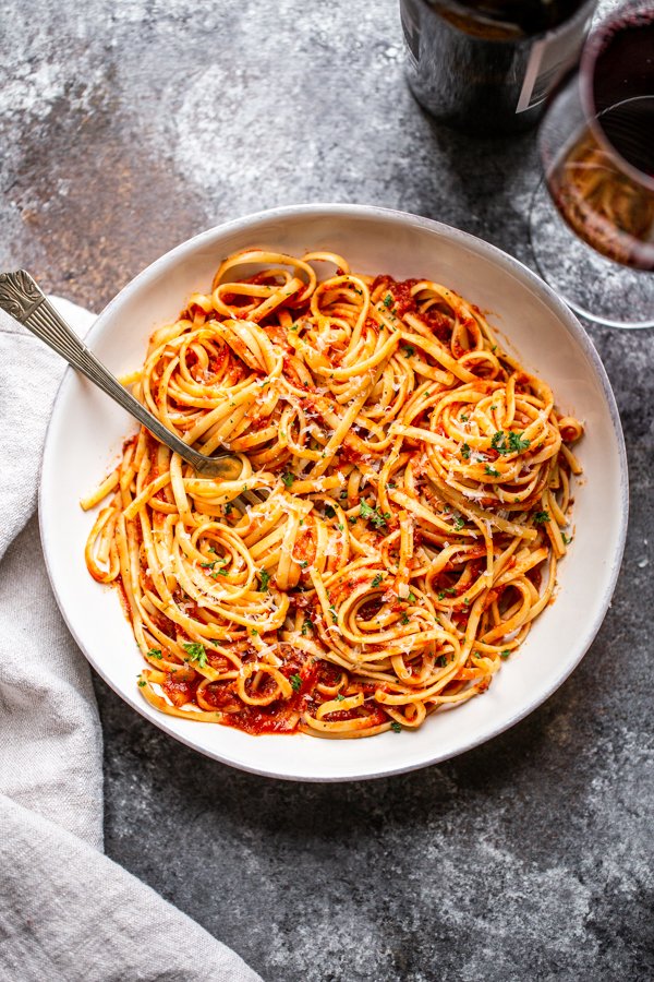 marinara sauce over pasta in a white bowl with wine and a napkin