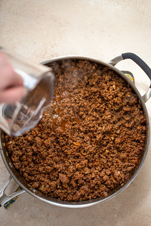 pouring water into taco meat in a pan