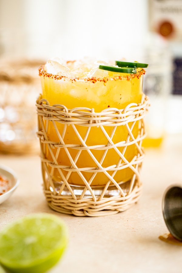 a jalapeno margarita in a rattan glass with a tajin rim
