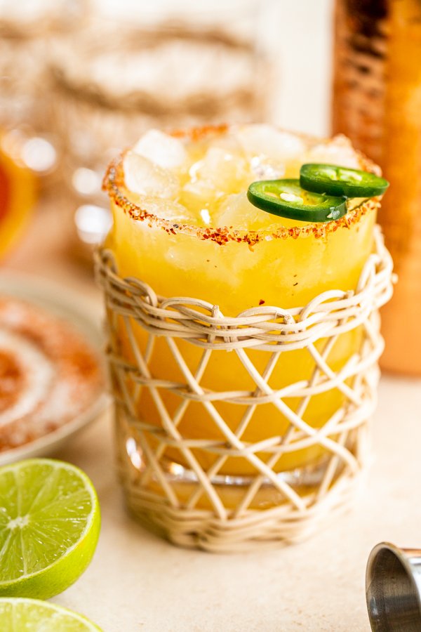 a jalapeno margarita in a rattan glass with a tajin rim