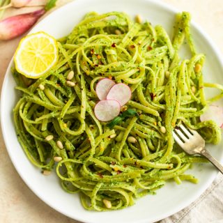 Plated fettuccini with radish pesto, a half of a lemon, and slices of radishes