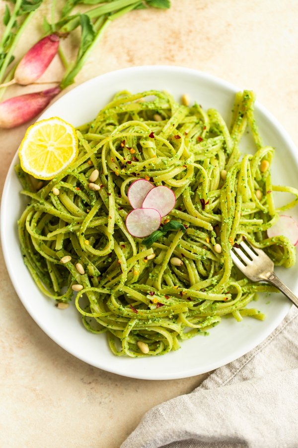 Plated fettuccini with radish pesto, a half of a lemon, and slices of radishes