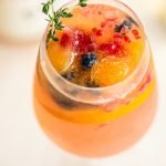 rose spritzer with berries filled ice cubes, rosemary sprig and berries