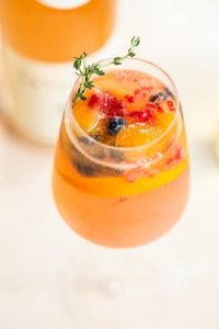rose spritzer in wine glass with fresh berries, berry filled ice cubes, and rosemary sprig