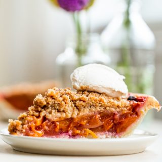 Slice of peach pie crumble topped with fresh whipped cream