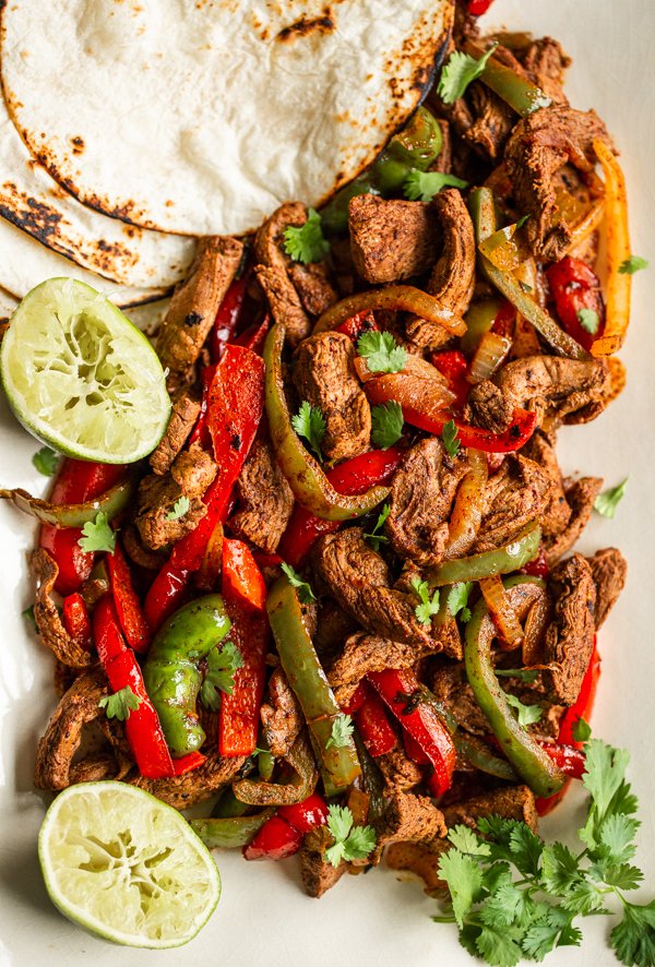 venison sliced in strips with sliced onion & red and green bell peppers, tortillas on the side and halved squeezed limes , topped with cilantro