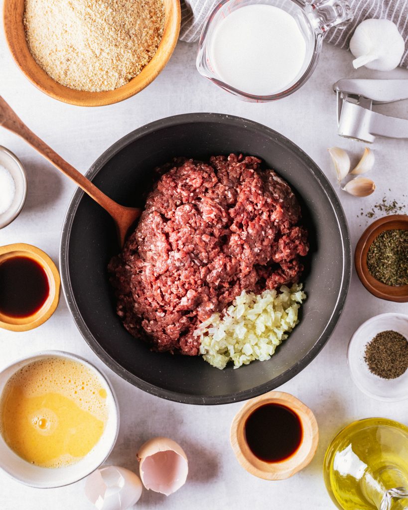 All of the ingredients for the venison meatloaf including a bowl of ground venison and chopped onion