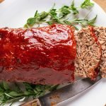 from above of sliced venison meatloaf on a white plate with a garnish