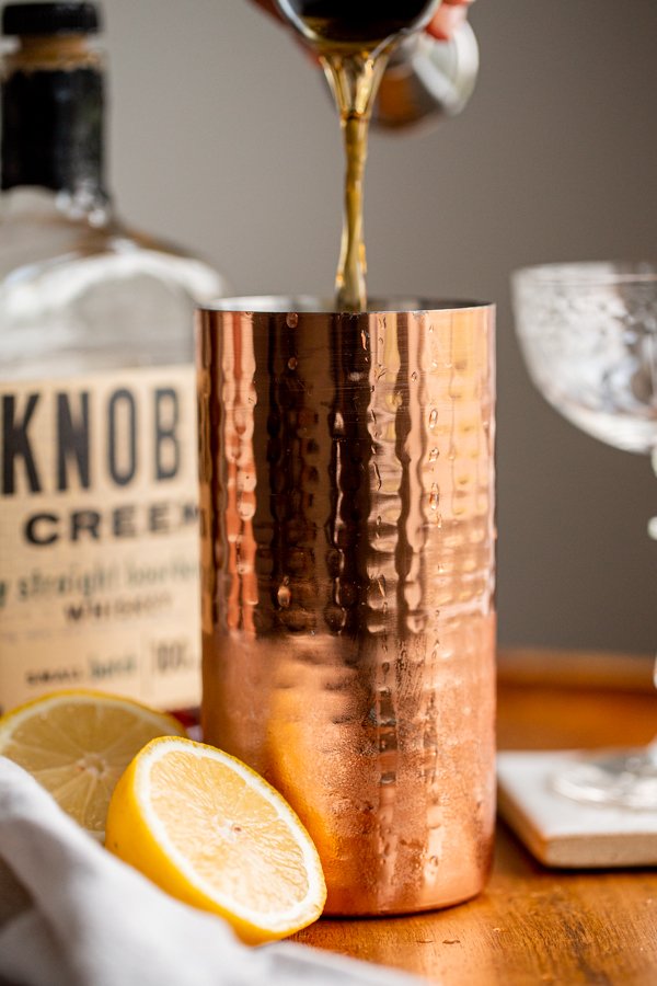 pouring a shot of bourbon into a cocktail shaker