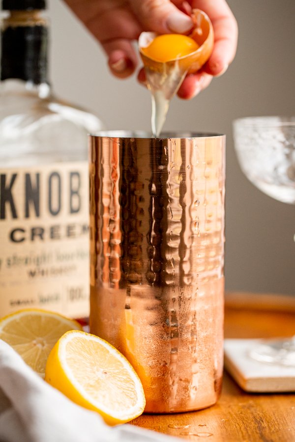 egg white being cracked into a cocktail shaker for a whiskey cocktail