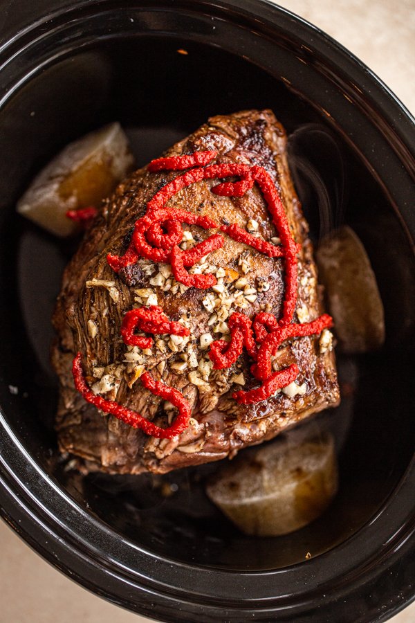 venison roast in crockpot topped with spices and tomato paste