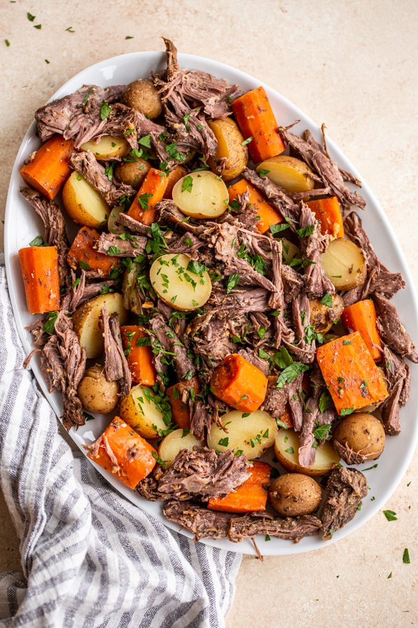 Venison roast, small yellow potatoes and diced carrots on a platter topped with parsley flakes