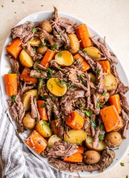 Venison roast, small yellow potatoes and diced carrots on a platter topped with parsley flakes