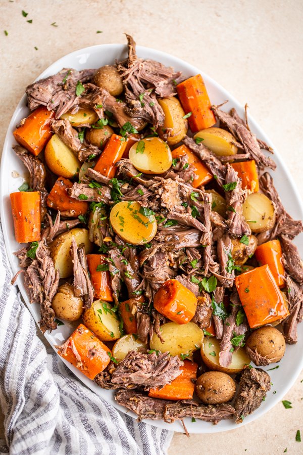 Venison roast, small yellow potatoes and diced carrots on a platter topped with parsley flakes