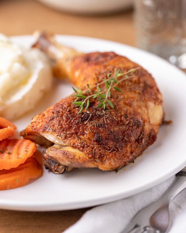 Whole roasted chicken legs with seasonings on a place with carrots and mashed potatoes 